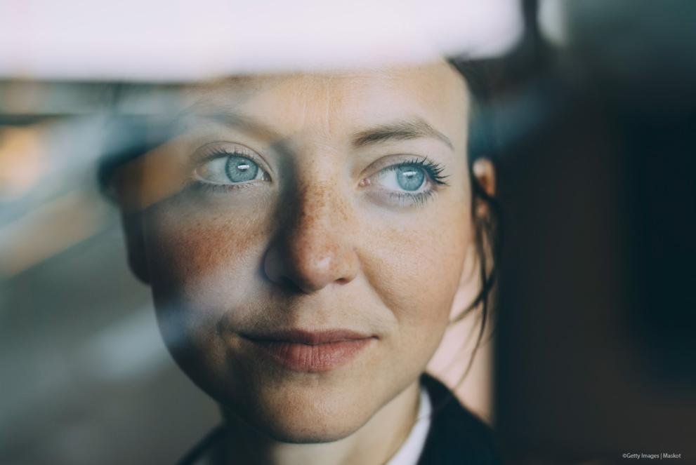 Thoughtful female executive looking away seen through glass at workplace